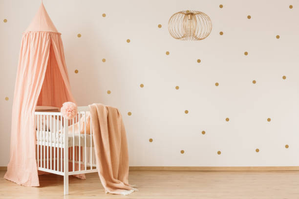 Blanket on crib Dirty pink blanket thrown on white wooden crib with canopy in simple baby room interior with dotted wall nursery bedroom stock pictures, royalty-free photos & images