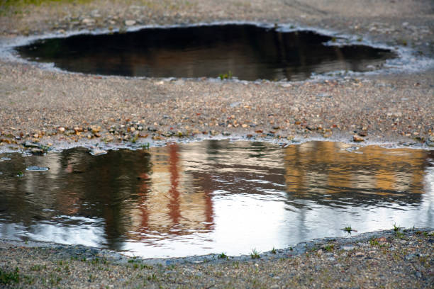 Road in bad conditions, row of buildings reflected on a pothole. Galicia, Spain.