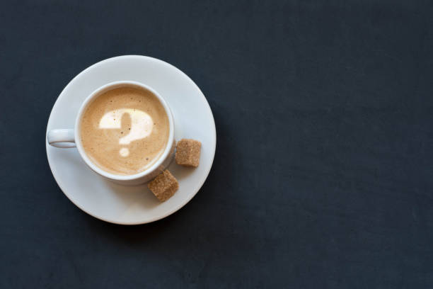 istock Cup of coffee with milk, cane sugar and question mark on dark background. Top view. Copy space 960985320