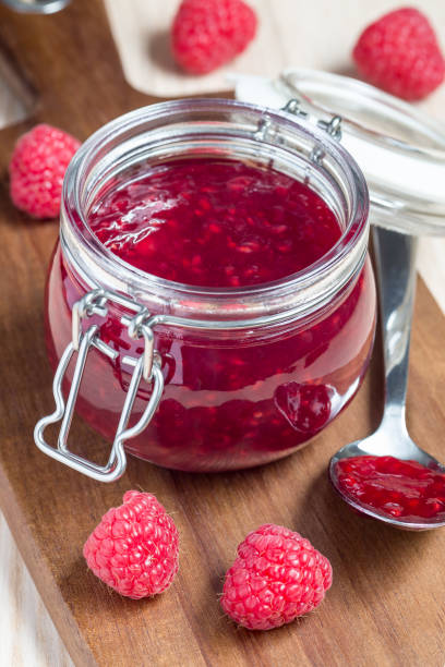 istock Raspberry jam in glass jar on a wooden board, vertical 961026516