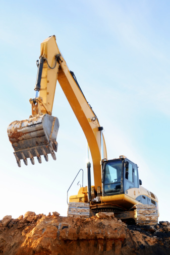 Yellow excavator loader at construction site with raised bucket over blue sky.