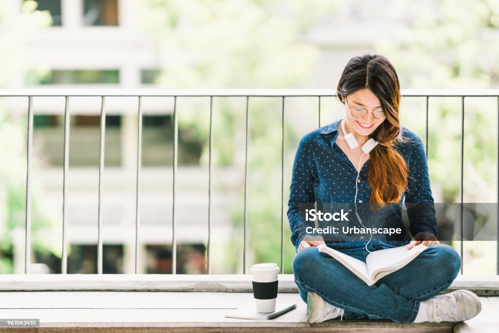 Young Asian college student girl reading book for exam, sitting at university campus with copy space. Education or casual studying lifestyle concept Reading Stock Photo