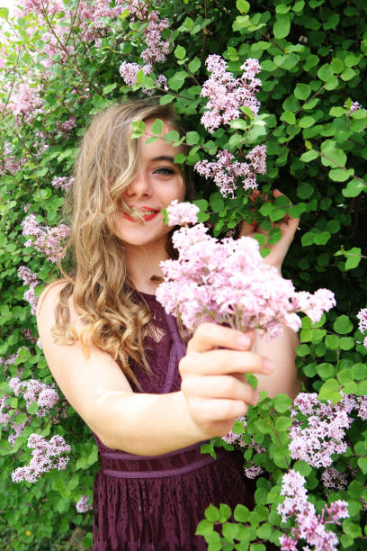 Teen girl surrounded by Dwarf Korean Lilacs (Syringa meyeri 'Palibin') and holding a small bouquet.   The Dwarf Korean Lilac blooms heavily in mid to late spring with showy clusters of fragrant pale lilac flowers.