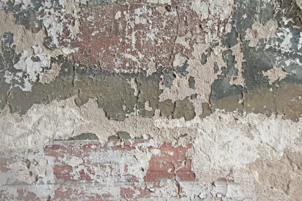 istock Old flaky white paint peeling off a grungy cracked wall. Cracks, scrapes, peeling old paint and plaster on background of old cement wall. An old cement stone wall as vintage cracked. Brick wall. 961052302