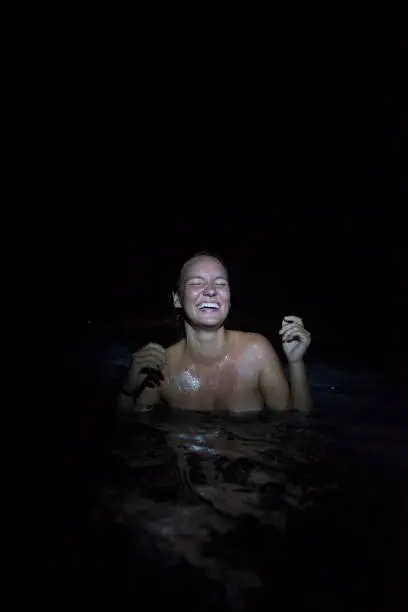 A young woman traveling in a rural area of Indonesia's Kalimantan laughs while taking a night swim in the pool beneath a small waterfall to bathe.