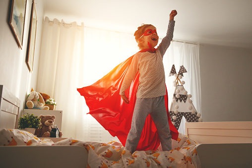 child girl in a super hero costume with mask and red cloak  at home