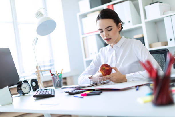 istock Young girl in the office working with documents and holding an apple. 961081200