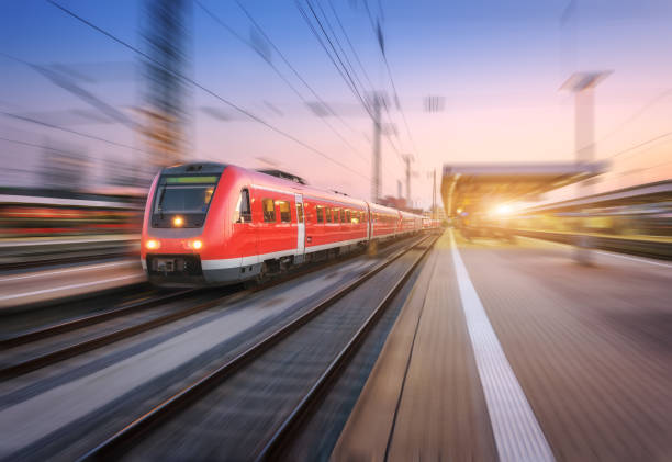 istock High speed red train with motion blur effect on the railway station at sunset. Landscape. Modern intercity train in motion on the railway platform at night. Commuter passenger train on railroad. Dusk 961081802