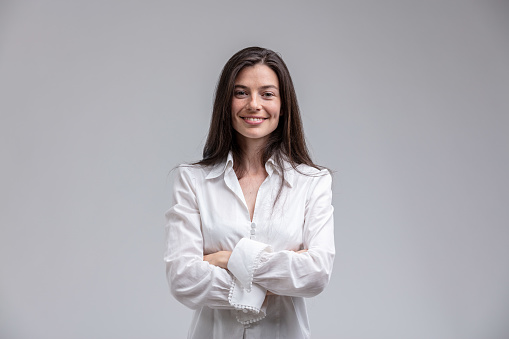 Portrait of long-haired brunette cheerful woman wearing white shirt standing with arms crossed