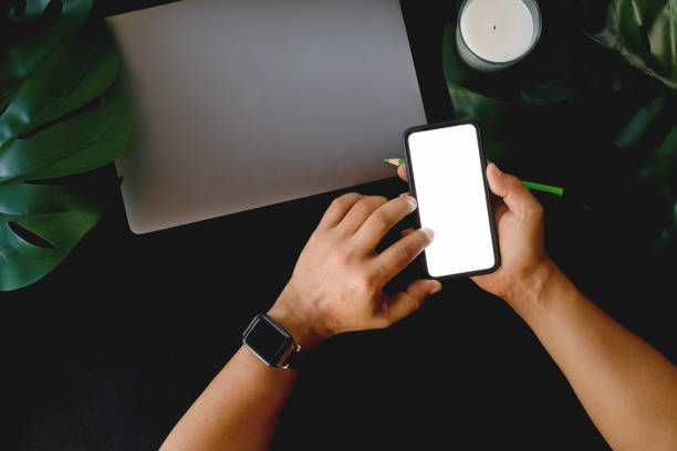 istock Man using mobile phone  on office dark leather desk table with supplies and coffee cup 961114074