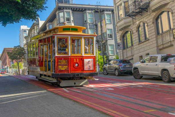A traditional San Francisco cable car traveling along a steep street lined with colorful residential buildings on a clear afternoon.