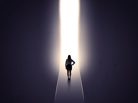 Young businesswoman stands in dark tunnel and looks in the glowing end