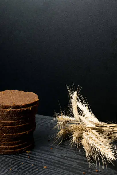 Rye bread, dark, fragrant, cut into thin round slices on a wooden background. Loaf of bread and rye ears still life on rustic background