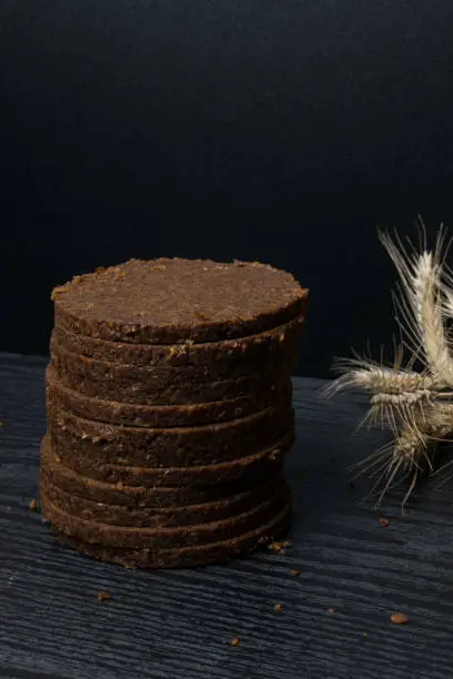 Rye bread, dark, fragrant, cut into thin round slices on a wooden background. Loaf of bread and rye ears still life on rustic background