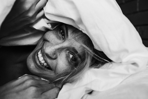 Portrait of a young beautiful woman waking up among the bed sheets, with a smile on her face