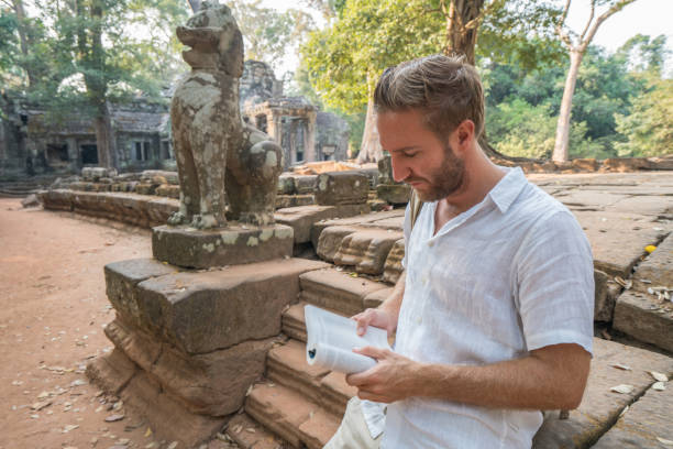 istock Young man reading guidebook at ancient temple in Cambodia 961209288