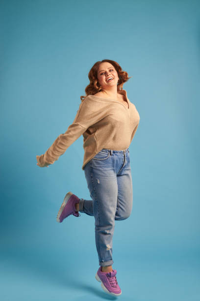 Plus-size woman jumping in excitement at studio Full-length shot of plus-size woman jumping in excitement at studio plus size woman fashion laughing stock pictures, royalty-free photos & images