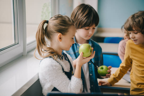 教室で一緒にティーン学童食べるリンゴ - child eating apple fruit ストックフォトと画像