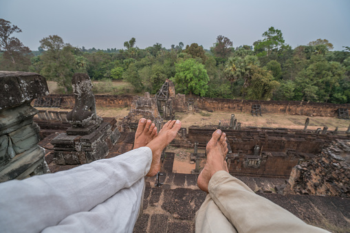 Personal perspective of couple sitting on temple's roof in Angkor Wat, close up on barefoot, sunset time. People travel concept.
Shot at Pre Rup temple, Angkor wat city, Siem Reap, Cambodia, Asia