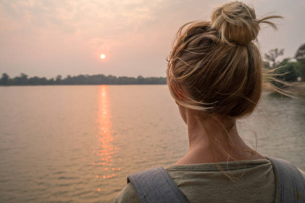 Photo of Young woman contemplating view at sunset from lakeside in Cambodia