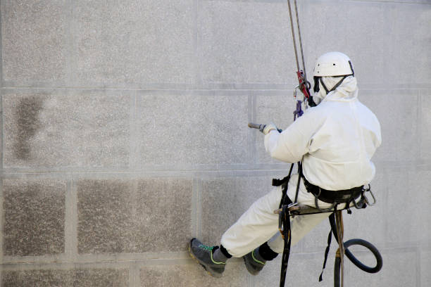 Worker wearing a protective gear cleaning a stone faceade in rope access stock photo