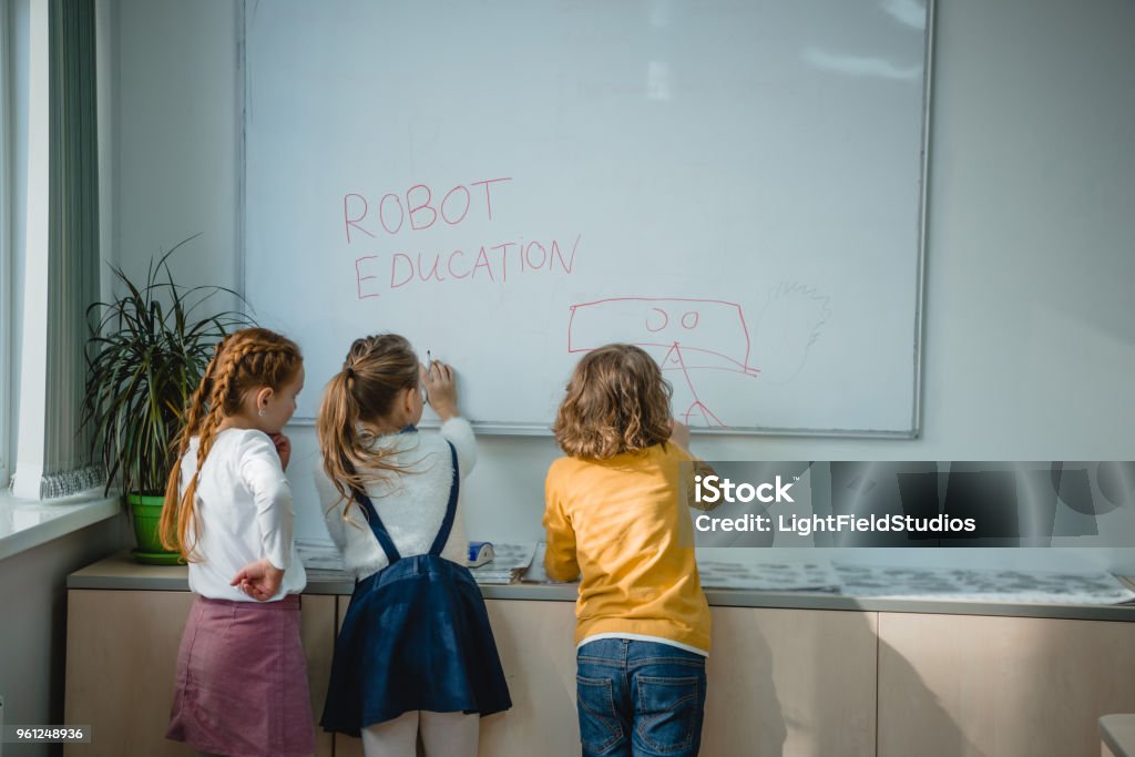 children writing and drawing  on whiteboard rear view of children writing and drawing robot education signs on whiteboard Elementary Student Stock Photo