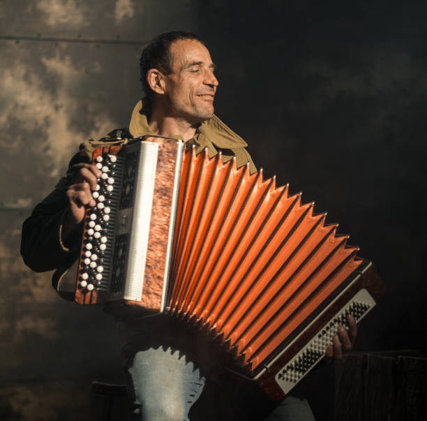 Cheerful Retro Artist Playing Accordion The mature caucasian man dressed in a military jacket with St. George ribbon on his chest. The man is sitting and playing an accordion a folk music. He smiling looking aside. Studio shooting accordion instrument stock pictures, royalty-free photos & images