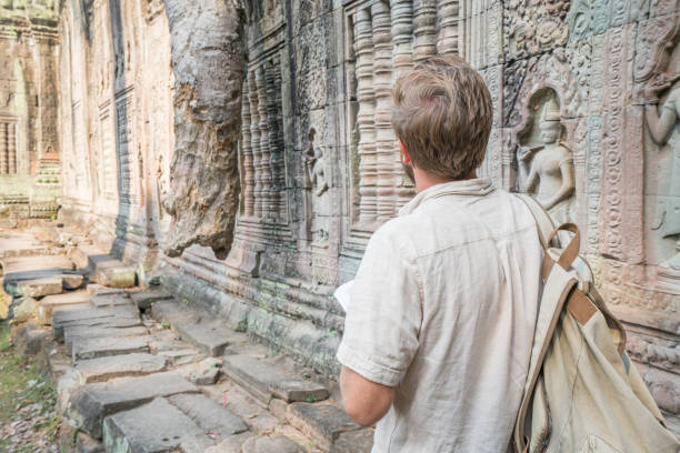 istock Young man reading travel guidebook at ancient temple in Cambodia 961260072