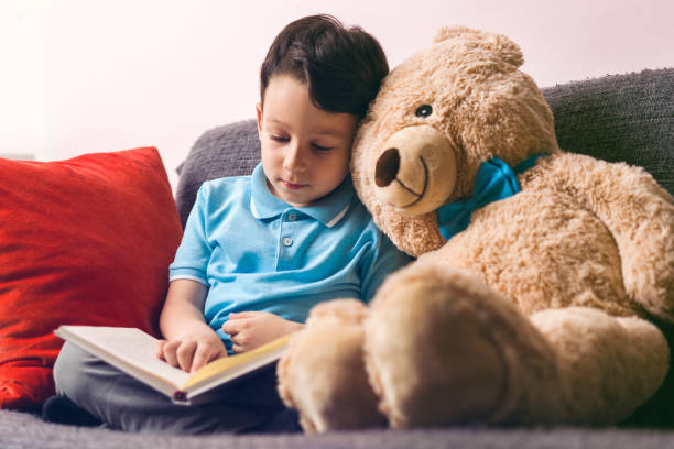istock Little boy is reading a book to his friend teddy bear. 961262018
