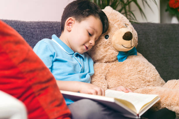 istock Little boy is reading a book to his friend teddy bear. 961262332