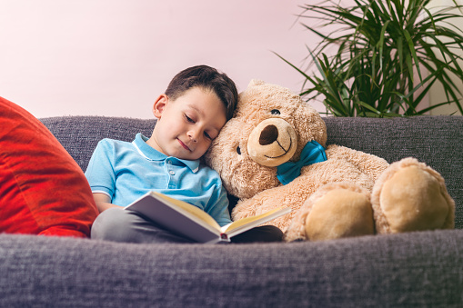 Little boy is reading a book to his friend teddy bear.
