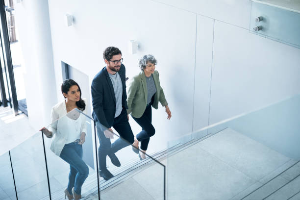 The go getters have entered the building Shot of a group of businesspeople walking up a staircase in an office steps stock pictures, royalty-free photos & images