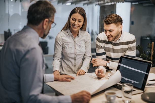 istock Happy couple analyzing blueprints with real estate agent in the office. 961270258