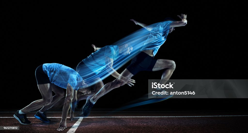 Male Athlete Running on Track The young caucasian man running on running track on black background. Studio shot. Sport and healthy lifestyle concept with strobe effect. Running Stock Photo
