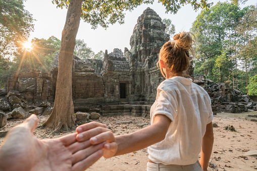 Follow me to concept, woman leading boyfriend to ancient temple, Cambodia. People travel concept.\nShot in Angkor Wat temples complex, Siem Reap, Asia, Southeast Asia.