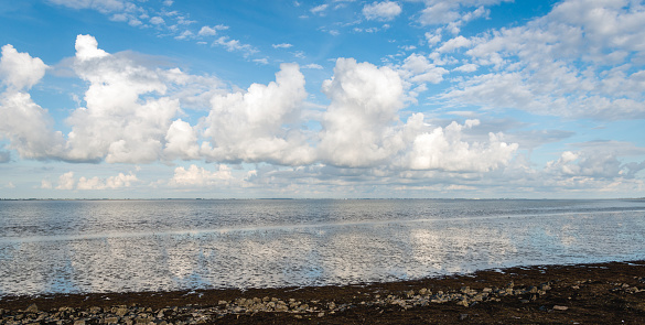 Beautiful sky with cumulus clouds reflected in the water surface of the Oosterschelde estuary. The photo was taken on a sunny day in the summer season at low tide from the Oesterdam between Zuid-Beveland and Tholen in the Netherlands.