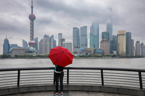 Woman with red umbrella enjoys the view to the skyline of Shanghai, China, on a rainy day