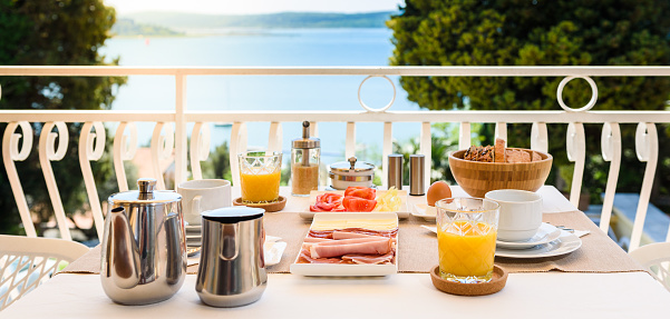Continental morning breakfast table setting with sea view is served. Hotel restaurant buffet breakfast is served on a balcony near the ocean. Vacation and travelling concept - Portoroz, Slovenia.