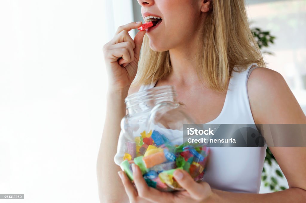 Pretty young woman eating colorful jelly candies at home. Addiction concept. Close-up of pretty young woman eating colorful jelly candies at home. Addiction concept. Candy Stock Photo