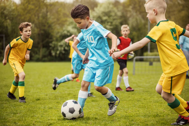 two boys soccer teams competing for the ball during a football match - childs game imagens e fotografias de stock