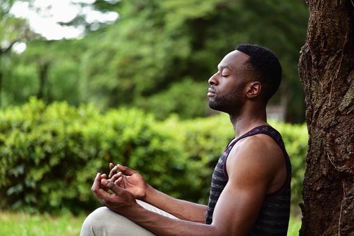 A young man sitting on the ground at a park, meditating.