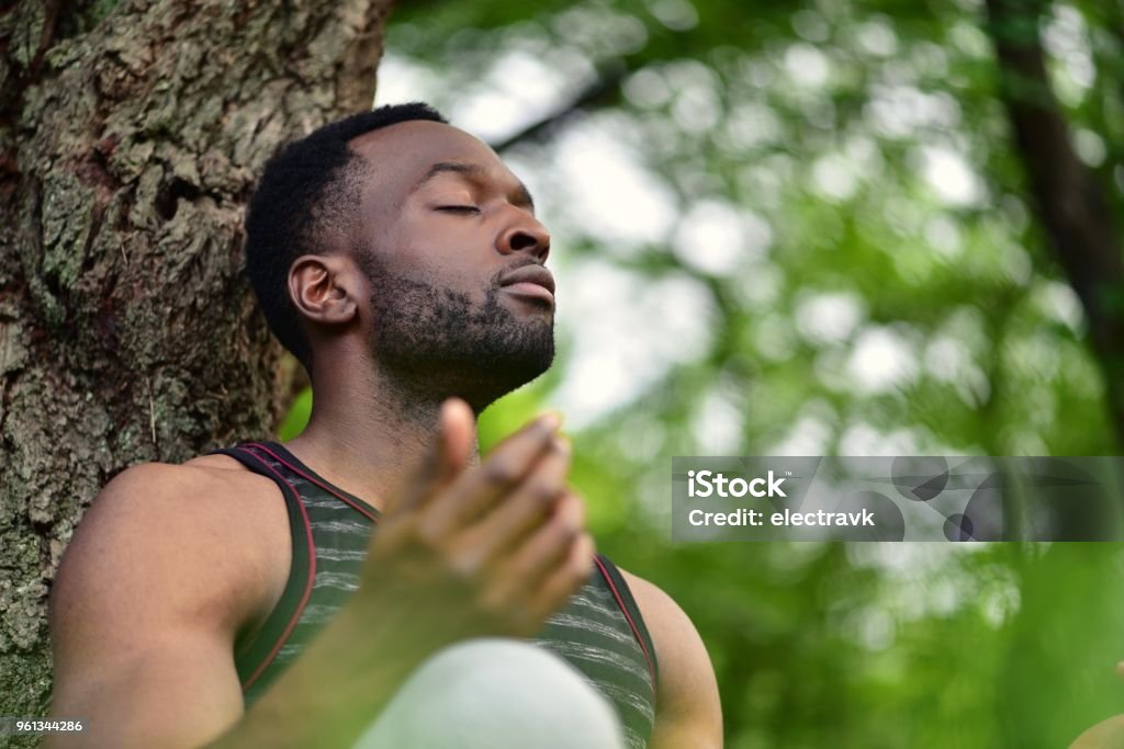 Young man meditating A young man sitting on the ground at a park, meditating. Only Men Stock Photo