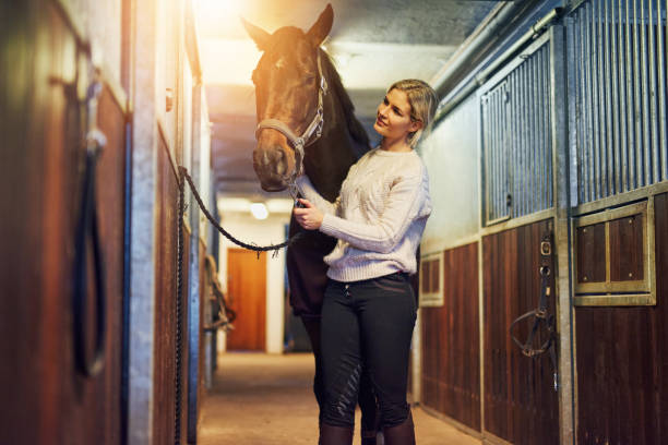 istock Smiling woman preparing her horse in stables before a ride 961361338