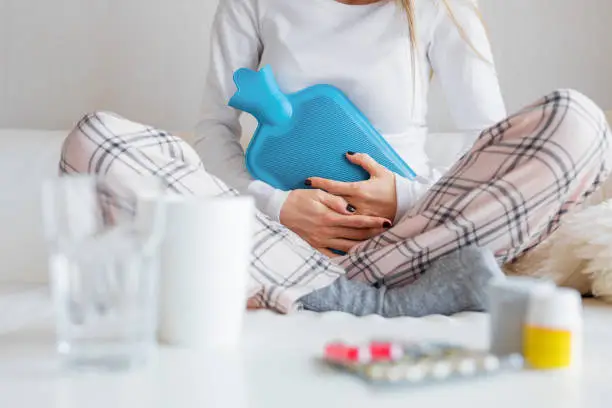 Close-up photography of unrecognisable woman with hot water bottle healing stomach pain.