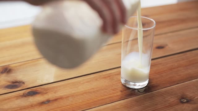 hand pouring milk into glass on wooden table