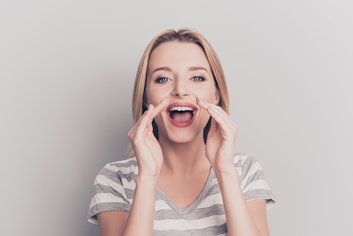 Portrait of pretty, caucasian, stylish, charming girl holding two hands near wide open mouth, shouting very loud, looking at camera, isolated on grey background