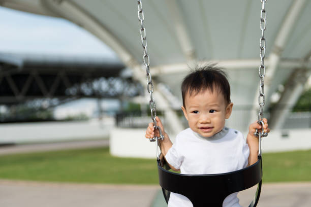 Adorable little Asian baby boy in swing at outdoor playground
