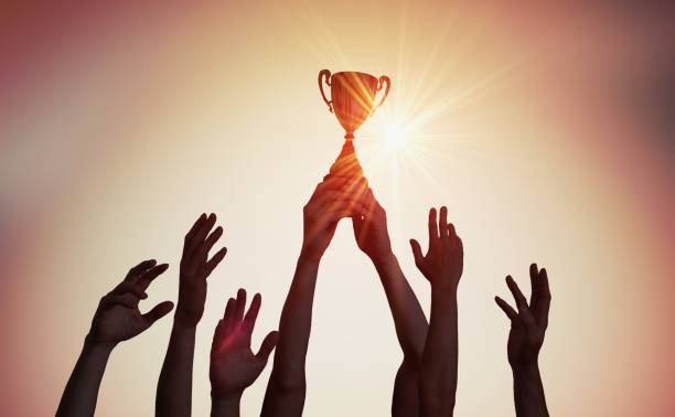 Winning team is holding trophy in hands. Silhouettes of many hands in sunset. Winning team is holding trophy in hands. Silhouettes of many hands in sunset. win prizes stock pictures, royalty-free photos & images