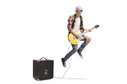 Teenage boy with an electric guitar plugged in an amplifier jumping isolated on white background