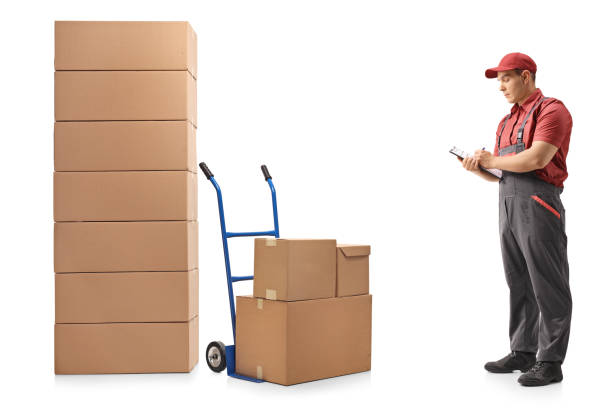 istock Mover standing next to a hand truck and a stack of boxes writing in clipboard 961399790